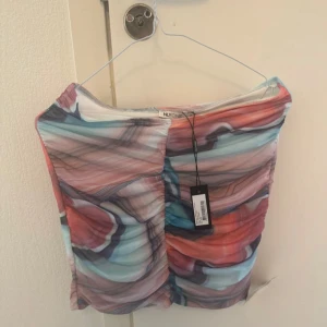 Flerfärgad set- mesh tubtopp och kjol från NLY One - Säljer en snygg tubtopp och kjol från NLY One i meshmaterial med färgglatt abstrakt mönster i rosa, blått, lila och vitt. Toppen är croppad och har tunna axelband. Perfekt för dig som vill sticka ut med en unik topp!