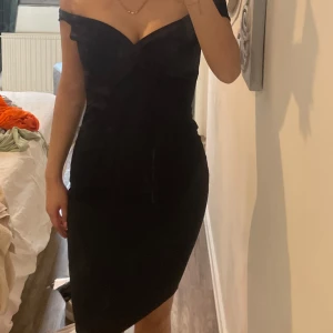 Svart offshoulder klänning - Säljer en svart, elegant klänning med offshoulder-modell och figurnära passform. Klänningen har en snygg v-ringning och asymmetrisk nederkant som ger en modern look. Perfekt för dig som vill sticka ut på festen! Helt ny också prislappen fortfarande på!
