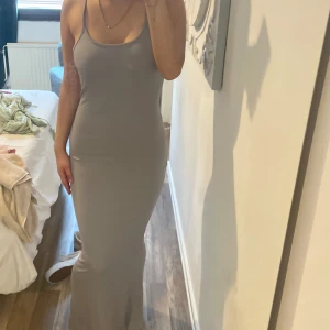 Ljusgrå långklänning med smala axelband - Säljer en enkel och stilren ljusgrå långklänning med smala axelband och figurnära passform. Perfekt för dig som gillar minimalistisk stil och vill ha något bekvämt men ändå snyggt.