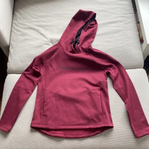 Vinröd hoodie från Peak Performance - Säljer en vinröd hoodie från Peak Performance i mjukt material. Tröjan har långa ärmar, huva med dragsko och diskret logga på bröstet. Perfekt för kyliga dagar och enkel att matcha med jeans eller tights. (För små för mig)