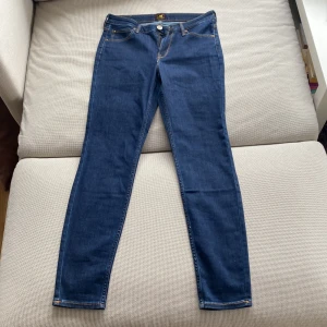Blå skinny jeans från Lee - Säljer ett par klassiska blå skinny jeans från Lee med fyra fickor och gul kontrastsöm. Byxorna har normal passform i midjan och smala ben. Perfekta till vardags och lätta att matcha med olika stilar. (För små för mig)