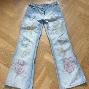 Ljusa jeans med broderade detaljer från Il Dolce - Unika ljusa jeans från Il Dolce med coola broderade mönster i olika färger. Byxorna har en avslappnad passform och vida ben, vilket ger en skön och trendig look. Perfekta för dig som vill sticka ut med en personlig stil. Köpta på 2000 talet och går inte att köpa längre💗passar mig som är 167 cm och 34 i midja