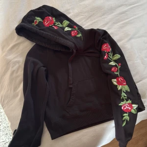 Svart hoodie från Hollister med rosbroderi - Snygg svart hoodie med vackra röda rosbroderier längs ärmarna och på huvan.