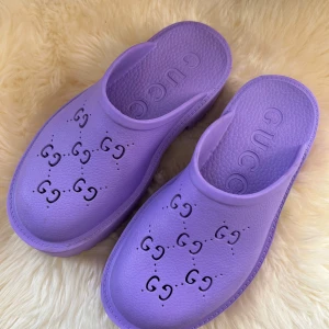 Lila tofflor från Gucci - Snygga lila tofflor från Gucci med det ikoniska GG-mönstret. Perfekta för en avslappnad stil med en touch av lyx. Tillverkade i syntetmaterial för komfort och hållbarhet.