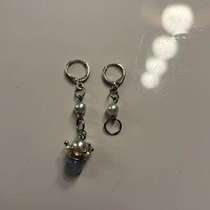 Silverörhängen med pärlor och blå sten - Snygga silverörhängen med hängande pärlor och en ljusblå sten i botten. Perfekt för att ge en elegant touch till din outfit. Den ena örhängen har en extra pärla och en blå sten med en kronliknande infattning.