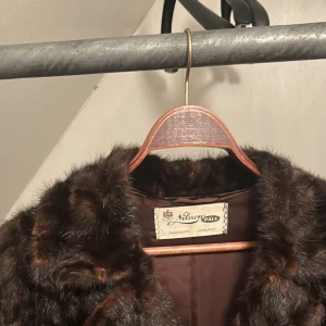 Brun pälsjacka från Nilssons Pals - Säljer en elegant brun pälsjacka från Nilssons Pals. Jackan har en lyxig känsla med knappar framtill och en vacker broderad insida. Perfekt för att hålla sig varm och stilfull under kalla dagar.