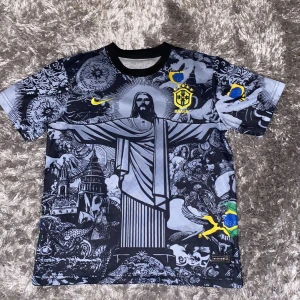 Fotbollströja med Brasilienmotiv - Snygg Brasilien fotbollströja. Tröjan har korta ärmar och är dekorerad med en stor bild av Kristusstatyn i Rio de Janeiro. Färgerna är främst svart och grå med inslag av gult och blått. Perfekt för fotbollsfans som vill sticka ut i sommar. Mitt pris är 500 då den är som ny men kan diskuteras. Skriv om ni har frågor💪🏽💯