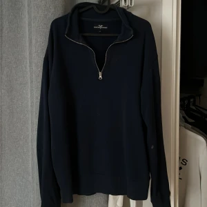 Mörkblå tröja med dragkedja från Hampton Republic - Säljer en stilren mörkblå tröja från Hampton Republic. Tröjan har en praktisk dragkedja vid halsen och långa ärmar. Perfekt för en avslappnad stil. 