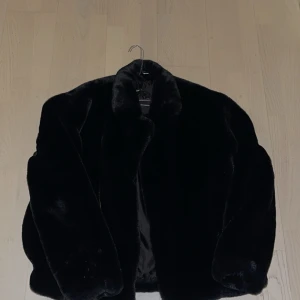 Svart pälsjacka (fuskpäls) - Säljer en elegant svart pälsjacka som är perfekt för kyliga dagar. Jackan har en klassisk design med långa ärmar och en mjuk, lyxig känsla. Den är både stilren och varm, vilket gör den till ett utmärkt val för vintern.
