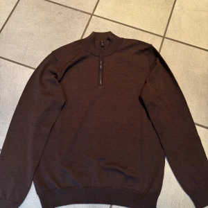 Mörkbrun tröja från Oscar Jacobson - Säljer en stilren mörkbrun tröja från Oscar Jacobson. Tröjan har en dragkedja vid halsen och är tillverkad i Italien. Perfekt för en elegant och avslappnad look. Tröjan är i merinoull vilket ger en bekväm passform. 