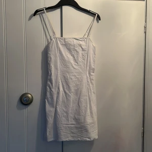 Vit klänning från BikBok - Säljer en stilren vit klänning från BikBok i storlek S. Klänningen har smala axelband och en dragkedja i ryggen för enkel påklädning. Perfekt för sommarens varma dagar!