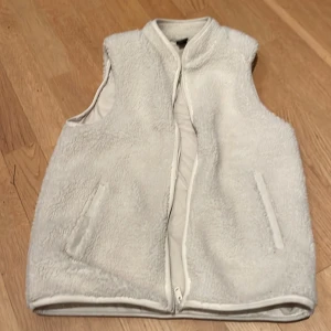Vit fleeceväst från SOC - Mysig vit fleeceväst från SOC med dragkedja framtill. Perfekt för kyliga dagar när du vill hålla dig varm och bekväm. Västen har en enkel och stilren design med två fickor på sidorna.