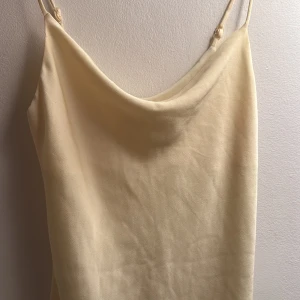 Ljusgul klänning från Gina Tricot - Säljer en elegant ljusgul klänning från Gina Tricot. Klänningen har smala axelband och en mjuk, flytande passform. Perfekt för en stilren look.