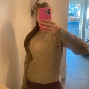 Beige stickad tröja från H&M - Säljer en mysig beige stickad tröja från H&M med ett subtilt hjärtmönster. Tröjan har långa ärmar och ribbade kanter vid hals, ärmslut och nederkant. Perfekt för kyliga dagar! 💛