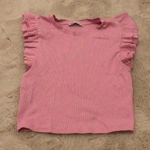 Rosa ribbad topp från Zara - Säljer en söt rosa ribbad topp från Zara med volangdetaljer vid ärmarna. Perfekt för en somrig look! 💖har dock två små fläckar på framsidan