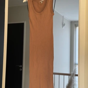 Beige/brun ribbad klänning - Säljer en stilren beige/gynnelnbrun ribbad klänning med ärmlös design. Perfekt för en avslappnad och chic look. Klänningen har en smickrande passform och är gjord i ett mjukt material.