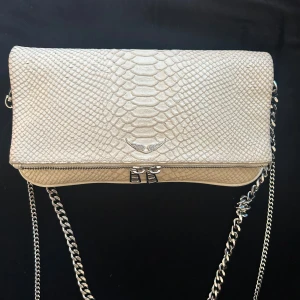 Zadig & Voltaire väska vit/krämvit - (Äkta) Knappt använd Zadig & Voltaire väska, en del av kedjan har trasslat sig lite, men det går att få upp om man vill, den har även några små fläckar på insidan. 28 cm på höjden och 14,5 cm på bredden. Köpt för 4000 kr. Kommer också med Zadigs egna dustbag om man önskar, pris kan diskuteras!