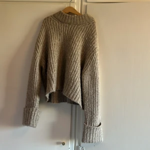 Beige stickad tröja från Gina Tricot - Säljer en mysig beige stickad tröja från Gina Tricot. Tröjan har en croppad design med långa ärmar och en hög krage. Perfekt för kyliga dagar när du vill vara både bekväm och stilren. Passar utmärkt till jeans eller kjol!