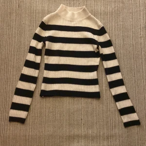 Randig ribbad tröja från H&M Divided - Säljer en stilren svartvit randig tröja från H&M Divided. Tröjan är ribbad med långa ärmar och en hög krage, perfekt för en trendig look. Passar bra till både jeans och kjol. 🖤🤍