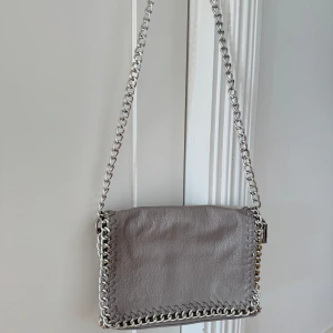 Grå axelväska från scorett, märke TIAMO - Grå axelväska från scorett med kedjeaxelband och dragkedja, inte kommit till användning därav nyskick! 