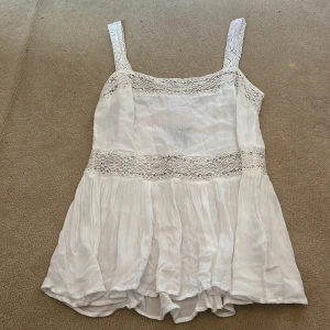 Vit blus med spetsdetaljer - Säljer en söt vit blus med spetsdetaljer. Den är ärmlös med breda axelband. Säljer den då jag aldrig har använt den och prislappen sitter kvar. Strl 40