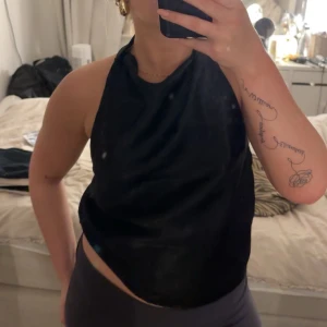 Svart halterneck topp - Snygg svart halterneck topp med öppen rygg. Perfekt för en stilren och modern look. Toppen har en enkel design som gör den lätt att matcha med olika outfits.