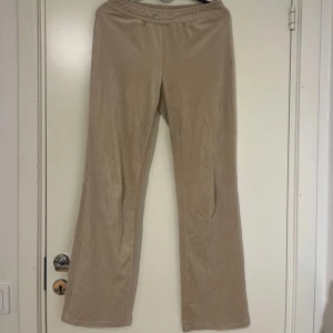 Beiga vida mjukisbyxor - Säljer ett par beiga mjukisbyxor med utsvängda ben och resår i midjan. Byxorna har en enkel och stilren design, perfekta för en avslappnad look. Materialet känns mjukt och bekvämt mot huden. Snörre saknas!!