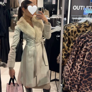 Kappa med krage i fuskpäls - Beige/krämfärgad kappa med avtagbar fuskpäls köpt från ASOS. Använd men i gott skick - inga hål eller liknande. Storlek 34 men passar även 36 då jag har 36 vanligtvis. 