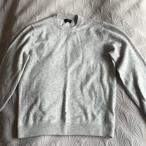 Ljusgrå merinoullströja från Massimo Dutti - Säljer en stilren ljusgrå tröja från Massimo Dutti i extra fin merinoull. Tröjan har rund halsringning, långa ärmar och ribbade muddar vid ärmslut och nederkant. Perfekt för lager-på-lager och enkel att matcha. Oanvänd och ny. Storleken är L men liten passform så skulle mer säga M.