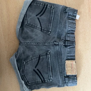 Grå jeansshorts med uppvikta ben - Snygga grå jeansshorts med uppvikta och fransiga benslut. Klassisk femficksmodell med dragkedja och knapp framtill. Bakfickor med dekorativa sömmar och läderpatch bak i midjan. Pris kan diskuteras.