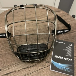 Bauer hockeygaller Profile III - Säljer ett Bauer Profile III hockeygaller i metall med svart vadderad hakrem och justerbara remmar. 