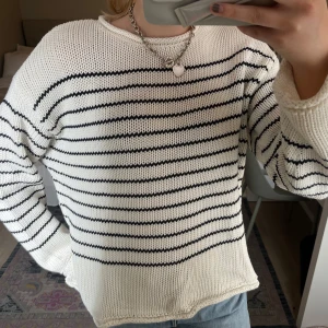 Blå och vit randig stickad tröja - Säljer en vit stickad tröja med blåa horisontella ränder. Tröjan har lång ärm och rund halsringning. Perfekt till jeans för en avslappnad stil.
