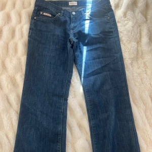 Blå jeansbyxor från Calvin Klein med strasstenar - Säljer ett par klassiska blå jeansbyxor från Calvin Klein med utsvängda ben och snygga strasstenar på bakfickorna. Byxorna har normal passform och femficksdesign. Perfekta för dig som gillar stilrena jeans med en twist. 