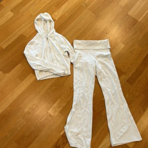 Vita mjukisbyxor från H&M med ribbad midja - Säljer ett par vita mjukisbyxor från H&M med bred ribbad midja och en matchade sip-up hoodie. Byxorna har en rak passform och är tillverkade i mjukt material som är skönt att ha på sig. Perfekta för en avslappnad stil.