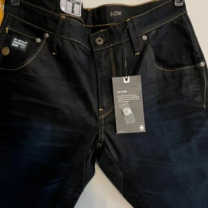 G-Star Arc 3D Slim jeans i mörkblå denim - Säljer ett par mörkblå G-Star Arc 3D Slim jeans i modellen Lexicon Denim. Byxorna har slim fit, snygga gula kontrastsömmar och klassisk femficksdesign. Perfekta för dig som gillar en modern och stilren look.