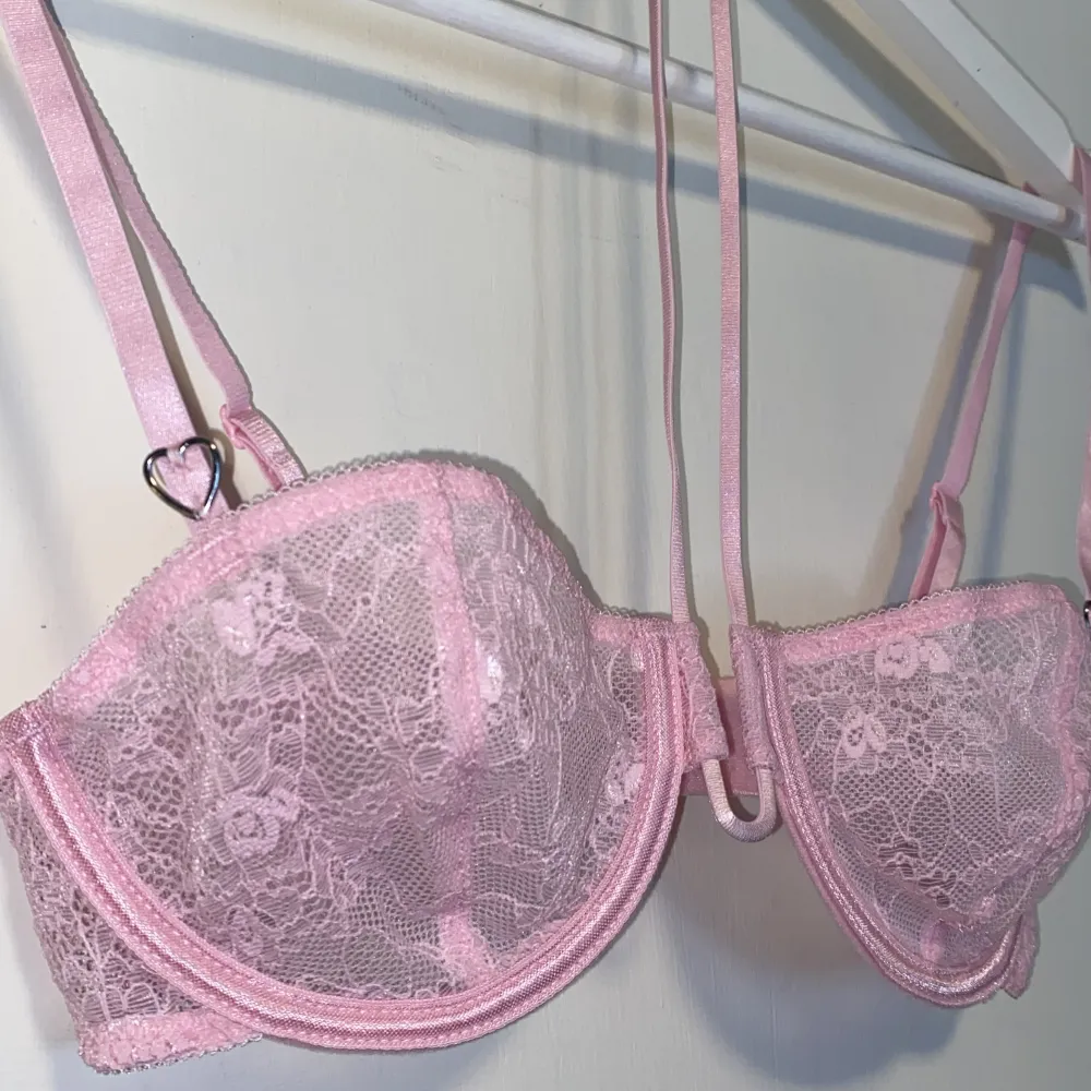 Säljer en söt rosa bh med spets, halterneckdesign och hjärtformade detaljer. Bh:n har justerbara band och vanlig knäppning bak. Den är aldrig använd men tvättrådet är bortklippt. Yläosat.