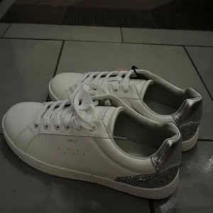Vita sneakers med silverdetaljer från ONLY - Snygga vita sneakers från ONLY med glittriga silverdetaljer på hälen. Helt oanvända med lappen fortfarande kvar, hör av dig vid frågor 💕