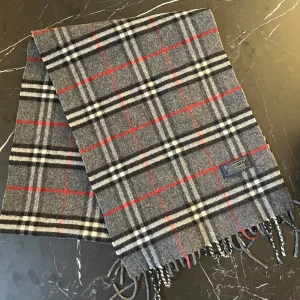 Grå rutig halsduk från Burberrys - Säljer en klassisk grå rutig halsduk från Burberrys i 100% kashmir. Halsduken har svarta, vita och röda ränder och är supermjuk och lyxig. Perfekt accessoar för att lyfta din outfi passar bra till sommar outfits mot kvällen. Säljer min för bara 1000kr🤩