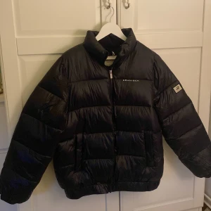 Svart pufferjacka från Röhnisch - Säljer en svart pufferjacka från Röhnisch med hög krage och dragkedja framtill. Jackan har en oversized passform och är vadderad för extra värme av hög kvalite. Perfekt för kyliga dagar och framförallt utomhus aktiviteter. Denna sitter verkligen sååå skönt på och håller dig verkligen varm , kvalitet på jackan är otrolig. Tyvärr så var denna lite stor i storleken och passade inte mig som bär storlek S, så skulle nog passat storlek M-L. Jackan är oanvänd och prislappen finns kvar. nypris: 2000kr