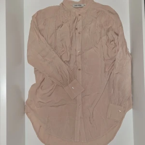 Beige skjorta/klänning från Carin Wester - Säljer en stilren beige skjorta/klänning från Carin Wester med klassisk krage och knäppning framtill. Skjortan har långa ärmar med manschett och rundad nederkant. Perfekt för en clean och avslappnad look. Hör gärna av dig vid frågor eller om du vill ha fler bilder!