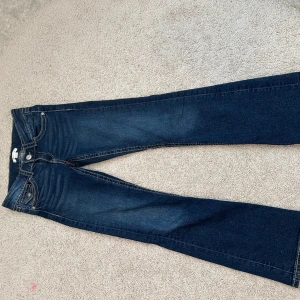 Mörkblå bootcut jeans med fickdetaljer - Snygga mörkblå jeans med bootcut passform och dekorativa fickor både fram och bak. Jeansen har kontrastsömmar och klassisk femficksdesign. Perfekta för dig som gillar en tidlös stil med lite extra detaljer. Fick de i present och har aldrig använt eftersom det inte var i min storlek 