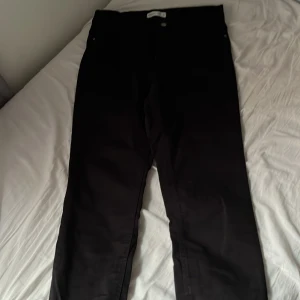 Svarta jeansbyxor - Svarta jeansbyxor med klassisk rak passform och normal midja. Byxorna har knapp och dragkedja framtill och är tillverkade i ett stadigt jeanstyg. Perfekta för en stilren och enkel look.