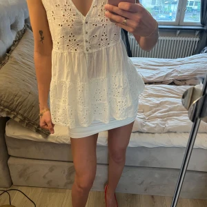 Vit ärmlös blus med broderade detaljer från KappAhl - Superfin vit blus från KappAhl med broderade blommor, knappar framtill och volang. Ärmlös modell med v-ringning och lätt a-linjeformad passning. Perfekt för sommarens alla tillfällen!