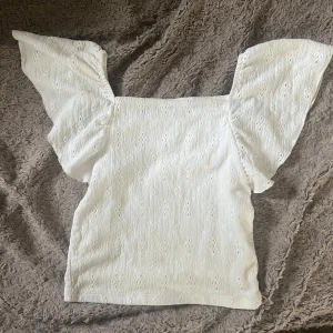 Vit blus  - Söt vit blus från Kappahl med broderade hålmönster och voluminösa korta ärmar. Fyrkantig ringning och lätt struktur i tyget ger en romantisk känsla. Perfekt för varma dagar och somriga outfits.