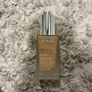 CAIA Dewy Drops Serum Foundation 20W - CAIA Dewy Drops Serum Foundation i nyansen 20W. Flytande foundation med silvrig pump och frostat glas. Ger en återfuktande och naturlig finish med lyster. Innehåller vitamin E och skvalan för extra vård.