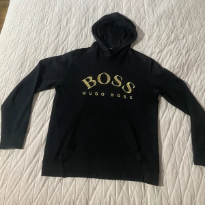 Hugo Boss Hoodie - Hugo Boss hoodie med guldig text storlek M. Är ganska använd som man kan se på bild 3 de är enda skadan.