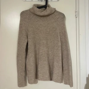Beige ribbad polotröja - Säljer en beige ribbad polotröja i mjukt material. Tröjan har lång ärm och hög polokrage, perfekt för kyliga dagar. Enkel och stilren design som passar till det mesta. Supermysig och varm!