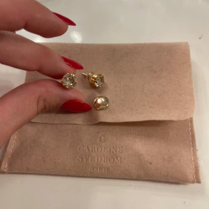 Guldpläterade örhängen - från Caroline Svedbom - Säljer ett par eleganta guldpläterade örhängen från Caroline Svedbom med stora, gnistrande klara kristaller. Perfekta för att ge en lyxig touch till din stil. Kommer med originalförpackning.