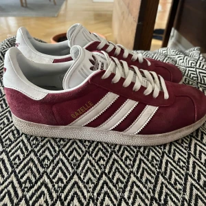 Vinröda Adidas Gazelle sneakers - Säljer ett par vinröda Adidas Gazelle sneakers. Har knappt använt dem så de är hela och rena utan några slitningar eller skador💞💞