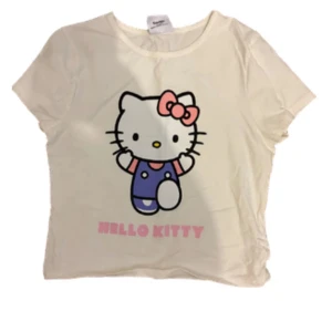 Vit Hello Kitty t-shirt - Säljer en söt vit t-shirt med Hello Kitty-tryck från Sanrio. T-shirten har korta ärmar och en rund halsringning. Perfekt för alla Hello Kitty-fans! 🐱🎀